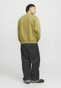 Olijfgroen sweatshirt met een ronde hals, losse pasvorm en geribbelde manchetten, gecombineerd met donkergekleurde denim broek en bruin schoeisel.