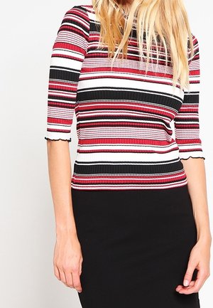 Donna che indossa un top aderente a maniche corte con righe orizzontali in rosso, nero, bianco e rosa, abbinato a una gonna nera.