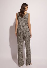 Kombinezon w czarno-białe wzory z dopasowanym górą i szerokimi nogawkami, zdobiony falistym wzorem i głębokim dekoltem na plecach w kształcie litery V.