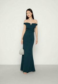 Vestido teal off-the-shoulder com corpete justo, saia fluida e decote em V. Acompanhado de uma pequena bolsa brilhante. Textura de tecido suave.