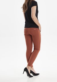 Úzké, měděné kalhoty s akcenty na zadních kapsách. V kombinaci s černým topem s krátkým rukávem a černými vysokými podpatky. Hladká textura.