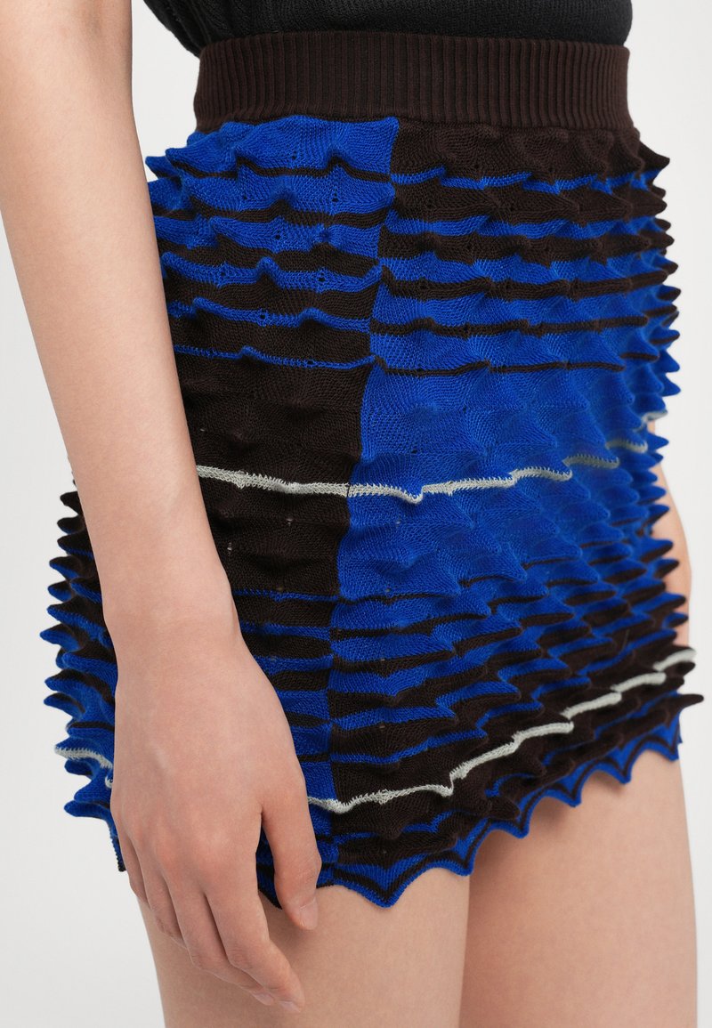 Gonna mini in maglia blu e marrone con design testurizzato e arricciato e una vita a costine. Presenta strisce alternate e una linea di accentuazione bianca.
