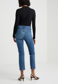 Svart ribbad långärmad topp kombinerad med högmidjade blå denimjeans, med rak snitt och bakfickor. Svarta högklackade sandaler.