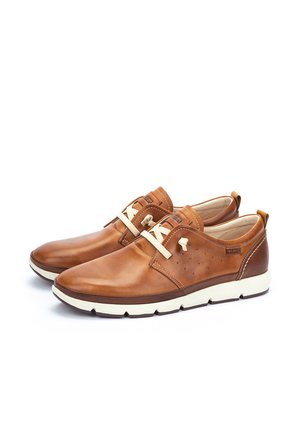 Casual bruine leren herenschoenen met crème kleurige veters, witte zolen en gestikte details, getoond vanuit een schuine zijaanzicht.