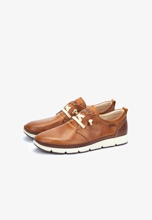 Chaussures en cuir marron décontractées pour homme avec lacets couleur crème, semelles blanches et détails cousus, vues sous un angle latéral.