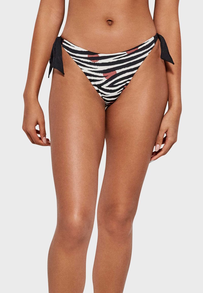 Bikini inferior con estampado de cebra en negro, blanco y rojo, con lazos laterales para un ajuste ajustable. Tejido suave con una textura lisa.