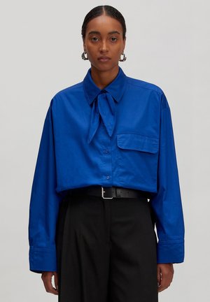 Blaues oversized Hemd mit einer Halsbindet, Knopfleiste, langen Ärmeln und einer Brusttasche; glatte Textur und lockerer Schnitt.