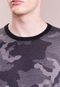 Maglione girocollo con colletto nero in grigio scuro con un motivo camo grigio chiaro. Realizzato in un tessuto lavorato a maglia liscio con una texture morbida.