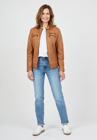 Bruine leren jas met een iets aansluitend ontwerp, twee borstzakken en geribbelde details. Gecombineerd met lichtblauwe jeans en witte schoenen.