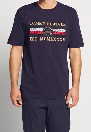 Navyblaue Baumwollt-Shirt mit rundem Ausschnitt, ausgestattet mit goldgesticktem Text und einem kreisförmigen Wappen auf gestreiftem Hintergrund.