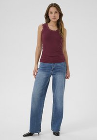 Haut sans manches bordeaux avec dentelle, associé à un jean bleu à jambes larges. Des escarpins noirs à bout pointu complètent la tenue.