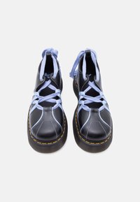 Bottes en cuir noir avec des lacets croisés violet clair, des coutures jaunes sur des semelles épaisses, vues de face sur un fond blanc.