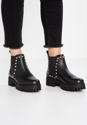 Bottes noires à la cheville avec une semelle épaisse, ornées de clous argentés sur les côtés. Fabriquées en cuir lisse à finition mate.