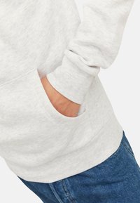 Grå sweatshirt med en subtil meleret tekstur, udstyret med en frontlomme og ribbede manchetter, parret med mørkeblå denimjeans.