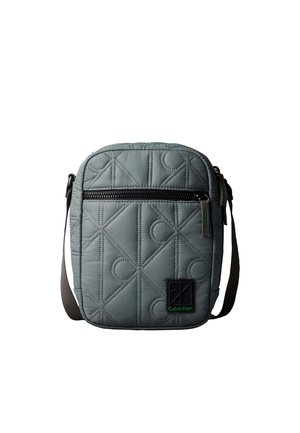 Sac à épaule matelassé gris avec poche zippée noire, bandoulière réglable et écusson logo Calvin Klein en bas à droite sur l'avant.