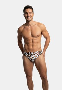 Bañador tipo slip en tela blanca con estampado de leopardo en negro y marrón. Presenta un ajuste ceñido y un pequeño logo bordado en la cintura.