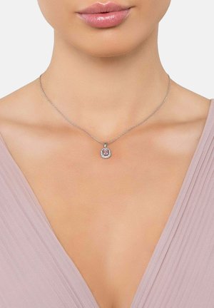 Frau trägt eine silberne Halskette mit einem quadratischen Anhänger aus pinkem Edelstein, umgeben von kleinen klaren Steinen, kombiniert mit einem blass mauvefarbenen V-Ausschnitt-Oberteil.