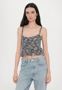 Kort topp i grått med melert mønster, med utringet hals og frynset kant, paret med høyt liv, lyseblå jeans.