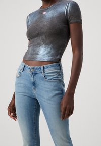 Metallic mörkgrå randig croptop med korta ärmar, tillsammans med ljusblå jeans i denim med klassisk femfickdesign.