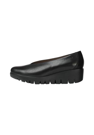 Zapatos de cuña de cuero negro con punta redondeada y suela dentada pronunciada. Diseño elegante con detalles mínimos.