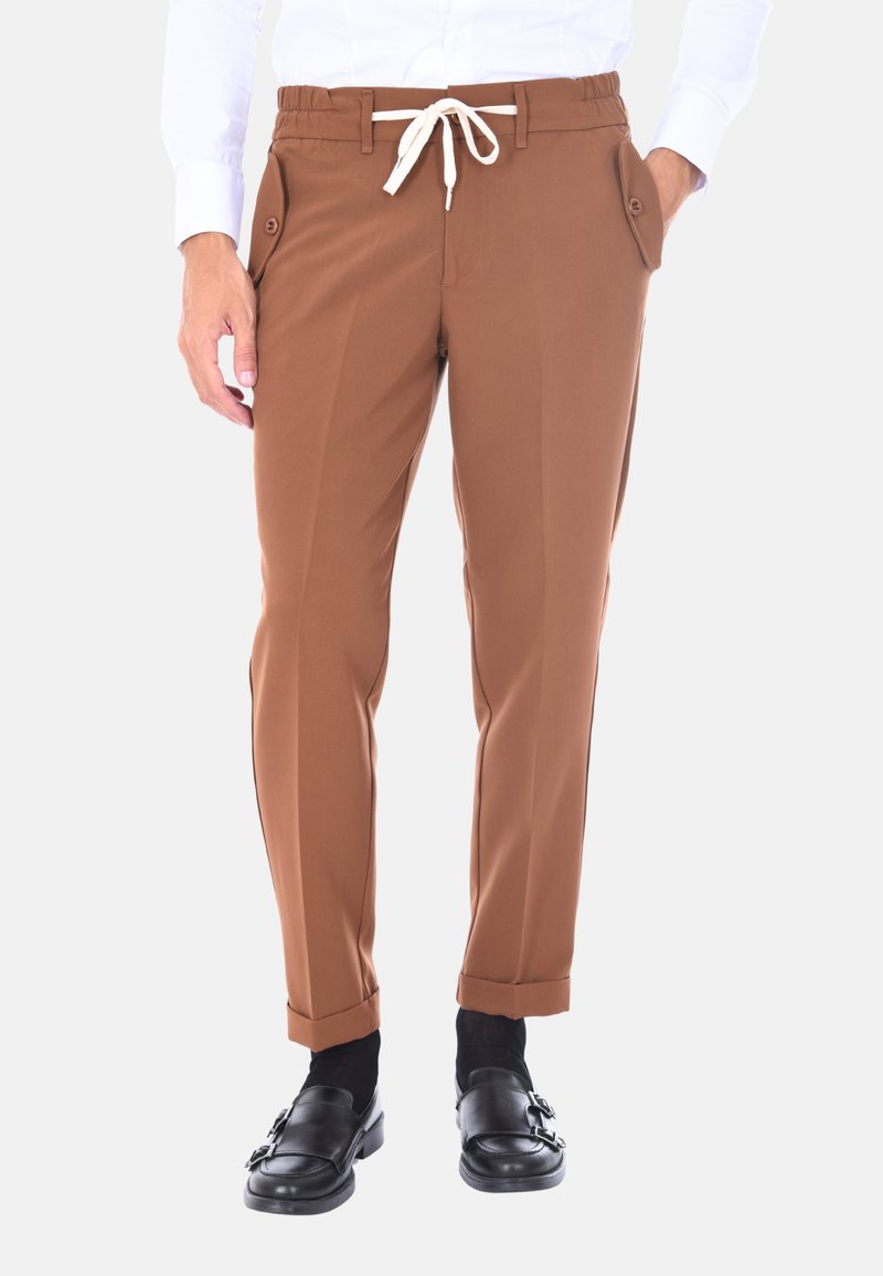 Pantaloni marroni a gamba affusolata in un tessuto liscio e elastico, con un elastico in vita, tasche laterali e maniche arrotolate. Abbinati a mocassini neri.