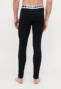 Schwarze Leggings aus dehnbarem Material, mit einem weißen Bund, der mit "JACK & JONES" gebrandet ist. Glatte Textur und figurbetontes Design.