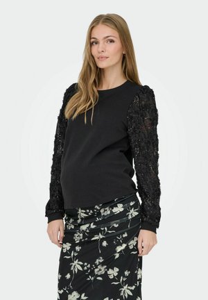 Svart tröja med texturerade puffärmar i svart tyg, matchad med en svart kjol med blommönster som har gröna och vita blommor.