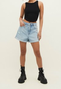 Czarny skrócony top na ramiączkach, jasnoniebieskie szorty dżinsowe z podwiniętymi mankietami i przetarciami, połączone z czarnymi, sznurowanymi butami na grubym obcasie.