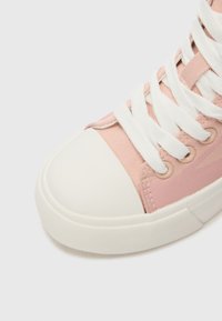 Ružová tkaninová vysoká športová obuv s bielym gumovým špičkou a podrážkou, ktorá má biele šnúrky a hladký povrch. Jemné detailovanie značky na boku.