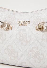 Bolso de hombro de lona blanca con un patrón texturizado, herrajes en tono dorado y un logo de la marca. Acentuado con broches decorativos y costuras.