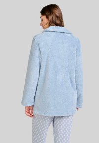 Chaqueta de forro polar azul claro, esponjosa, con cuello de muesca y mangas largas. La tela tiene una superficie suave y texturizada. Sin cierres visibles.