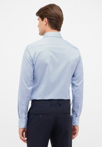 Camicia a maniche lunghe con bottoni di colore azzurro chiaro e motivo geometrico. Realizzata in tessuto dalla texture liscia; presenta un colletto classico e polsini con bottoni.