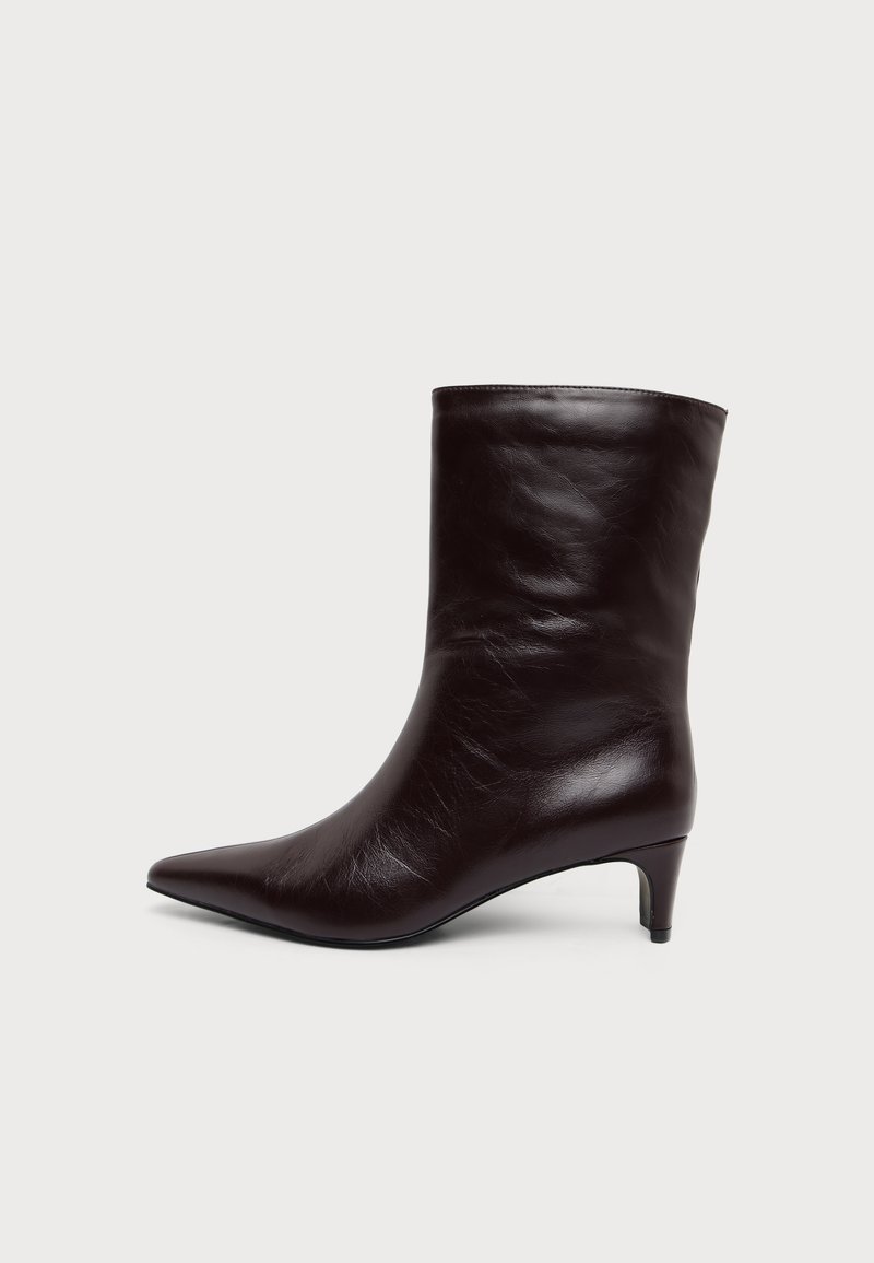 Bottine en cuir marron foncé avec bout pointu et petit talon kitten sur un fond clair uni.