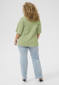 Green textured top with short sleeves, paired with light blue straight-leg jeans and black heeled sandals, viewed from the back.