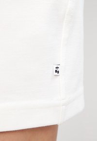 Lähikuva valkoisesta kankaasta, jossa on pieni etiketti, jossa on musta kirsikkalogo ommeltuna sauman lähelle alareunassa.