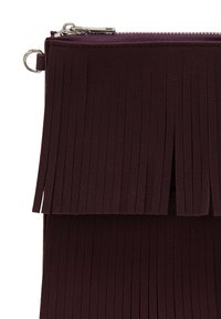 Burgundowa torebka z sztucznej skóry z pionowymi frędzlami, z zamkiem błyskawicznym na górze i pierścieniowym uchwytem po boku.