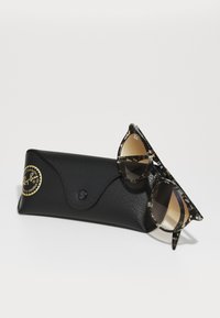 Gafas de sol Ray-Ban con montura de carey de patrón y lentes marrones degradados, colocadas sobre un estuche de cuero negro con un logotipo circular.