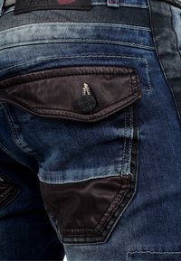 Jeans en denim bleu foncé avec des accents de poches en cuir texturé, des coutures contrastantes et un design de poche unique avec un bouton de marque.
