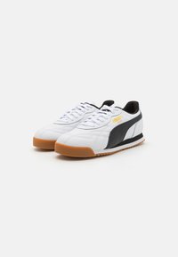Hvide sneakers med sort sidepanel og gul logo. Lavet af struktureret læder, med hvide snørebånd og en gummigummisål.