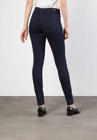 Mørkeblå jeans med slim fit, med baklomme, synlig søm og høy midje. Brukt med svarte hæler.