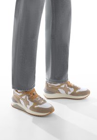 Sneaker bianchi e marrone chiaro con texture in suede e mesh, caratterizzati da un design a stella prominente, lacci beige e una spessa suola bianca.