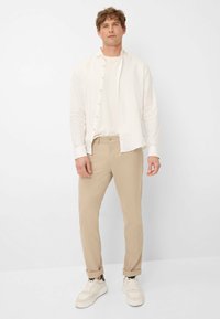 Beige broek gecombineerd met een witte linnen longsleeve shirt en witte sneakers. De outfit is casual met een losse pasvorm en opgerolde mouwen.