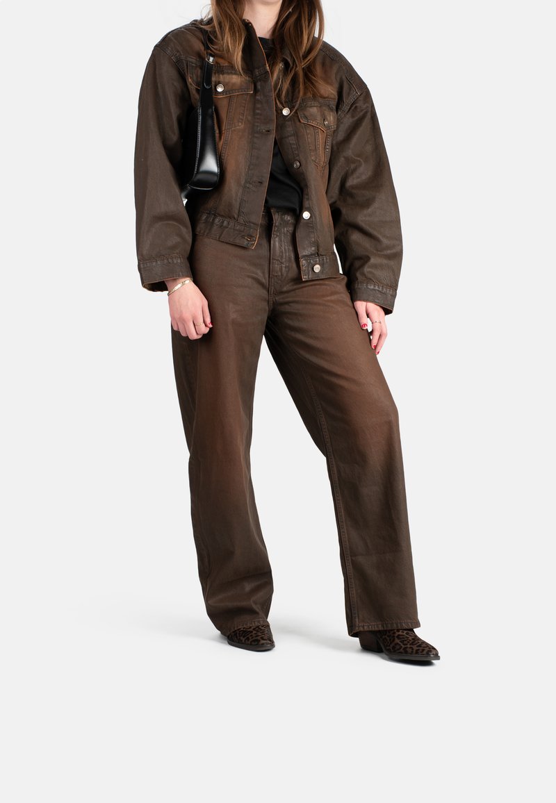 Chaqueta de mezclilla marrón con un corte relajado, combinada con pantalones de pierna ancha marrones a juego. Un bolso negro y botas de tobillo con estampado de leopardo complementan el atuendo.