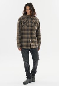 Geruite flanellen shirt in bruin en zwart, met twee borstzakken, knoopsluiting en lange mouwen, gecombineerd met donkere spijkerbroek en laarzen.
