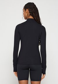 Czarna bluzka z długim rękawem i stójką, wykonana z teksturowanego materiału, o dopasowanym kroju, z otworami na kciuki na mankietach, zestawiona z czarnymi szortami.