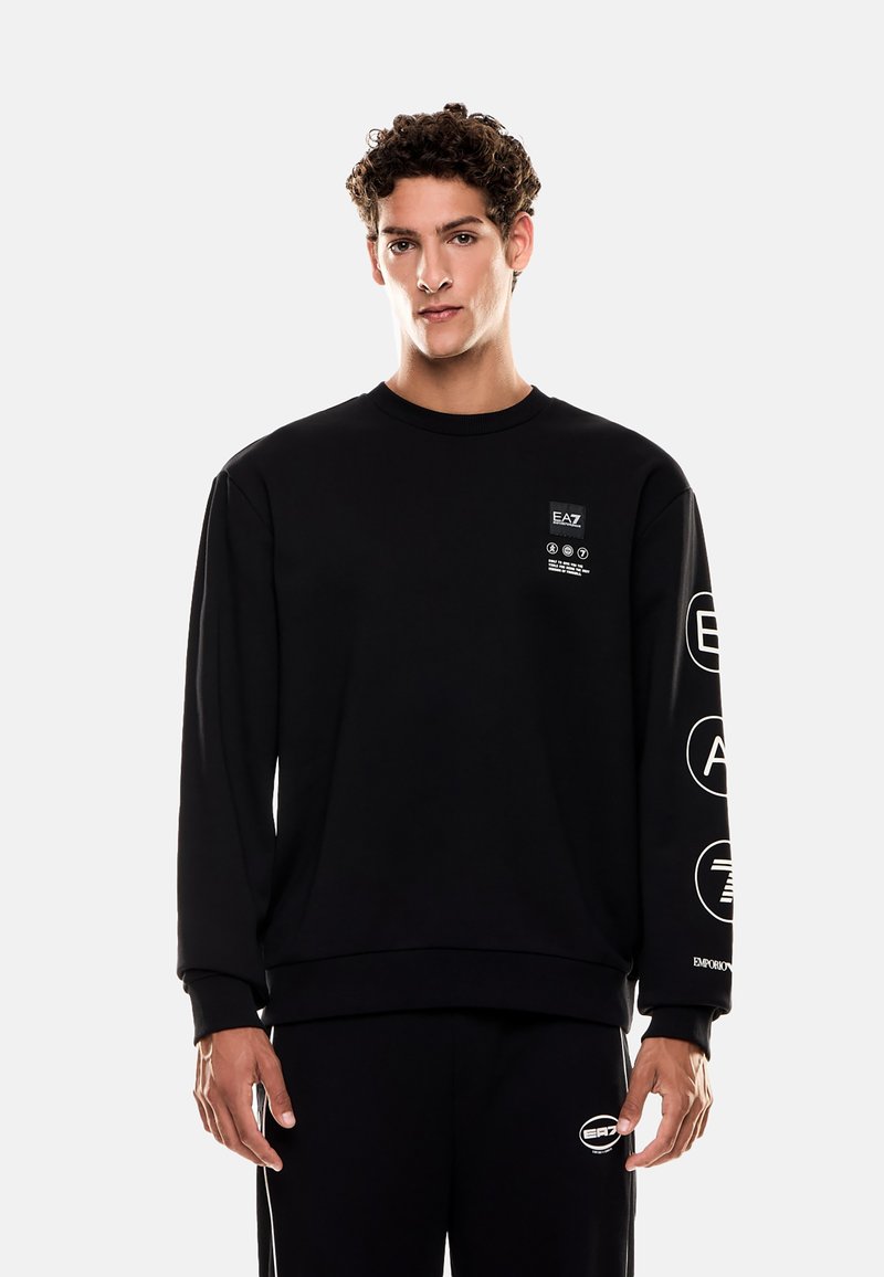 Černá mikina s kulatým výstřihem, s bílými grafickými doplňky na hrudi a levém rukávu. Vyrobena z měkké, texturované látky.