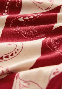 Red and cream fabric featuring a pattern of swans, hearts, and soft texture with visible folds and a smooth appearance.