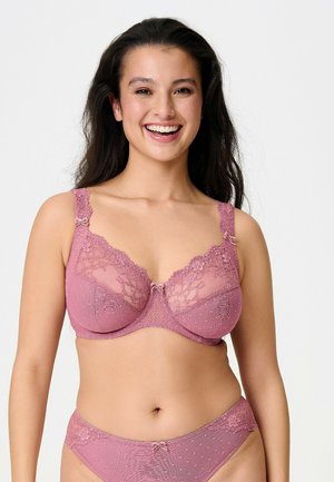 Donna sorridente con lunghi capelli scuri che indossa un coordinato in pizzo color malva composto da reggiseno e slip, su uno sfondo chiaro e uniforme.
