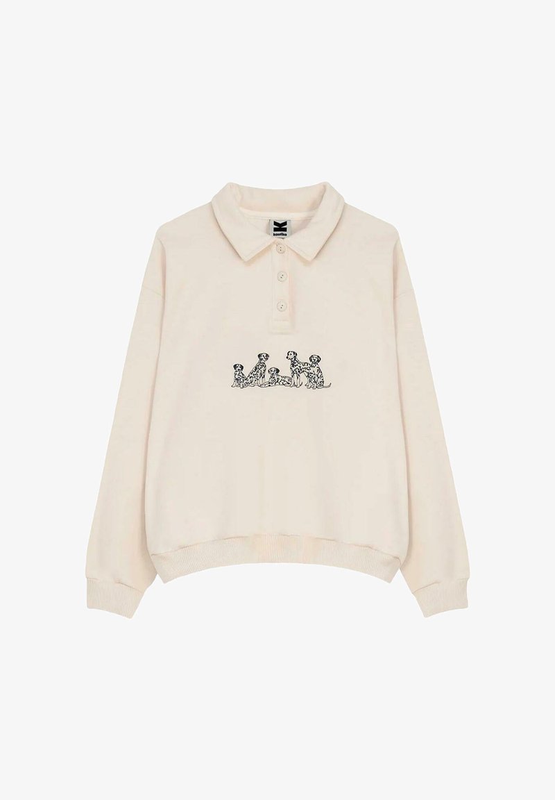 Suéter tipo polo color crema con cuello, que presenta un gráfico de un perro negro en el frente. Hecho de tela suave con puños y dobladillo acanalados.