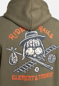 Sweat à capuche vert olive avec un graphique représentant un chien cartoon portant un chapeau, des bûches croisées et un sac. Le texte indique "RIDE THE RAILS" et "ELEMENT & TIMBER."